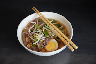 A sleek bowl of vibrant mung bean noodle soup with vegetables and protein, styled on a minimalist light background.