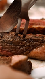 Chef slicing into a thick, tender steak with a knife and fork, steam rising invitingly.