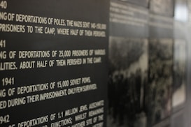 A close-up view of a wall display featuring historical text about deportations during World War II. The focus is on large, bold white text on a dark background, detailing numbers of deported individuals and their fates. Partially visible are blurred black-and-white photographs accompanying the text.