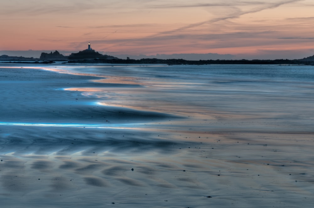 a view of a beach at sunset with a lighthouse in the distance