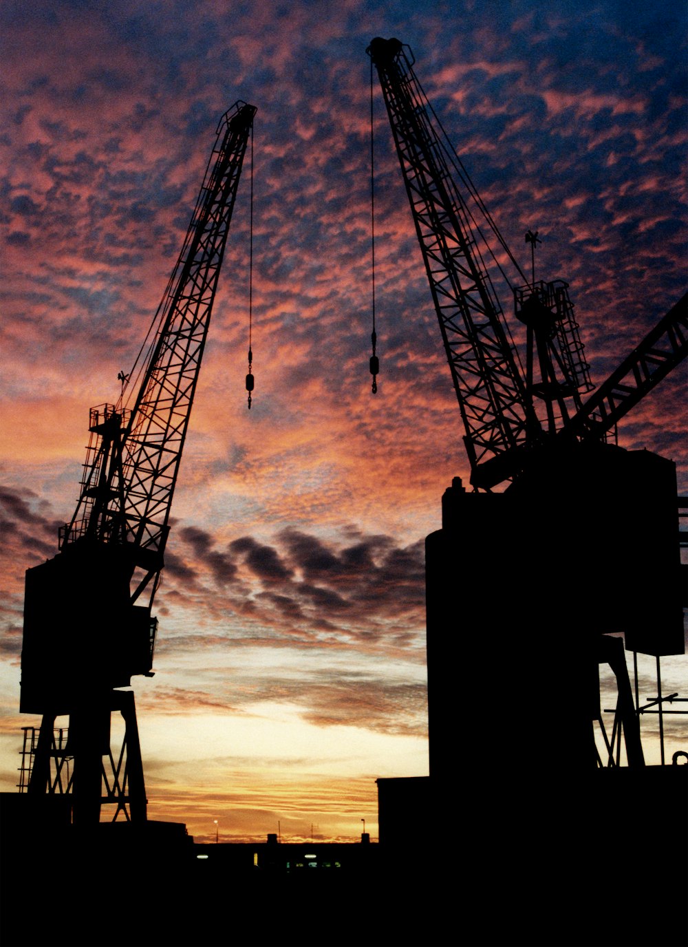 two cranes are silhouetted against a sunset sky