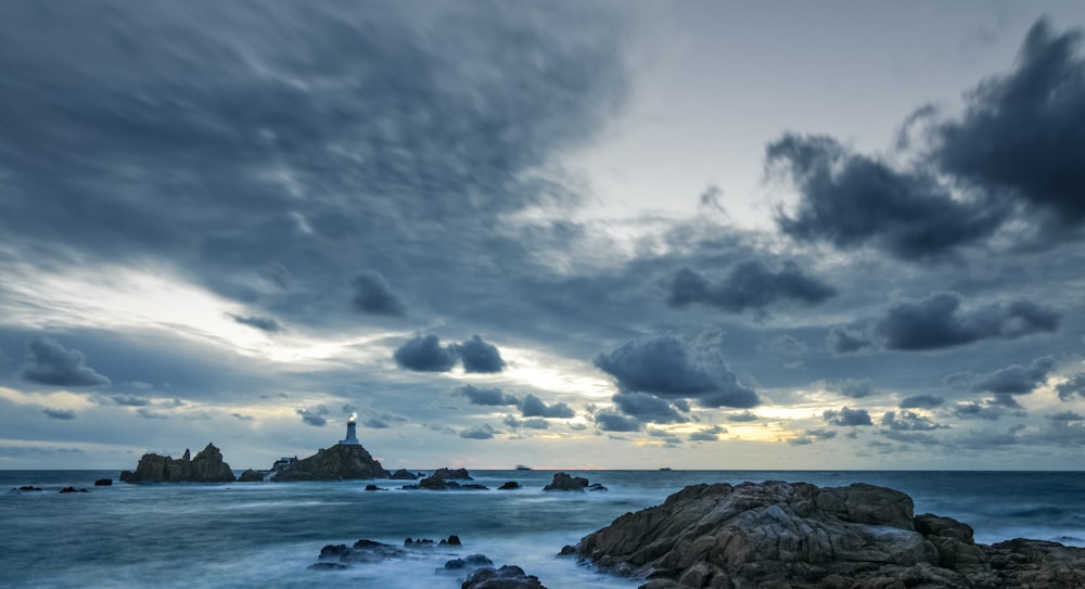 a cloudy sky over the ocean with a lighthouse in the distance