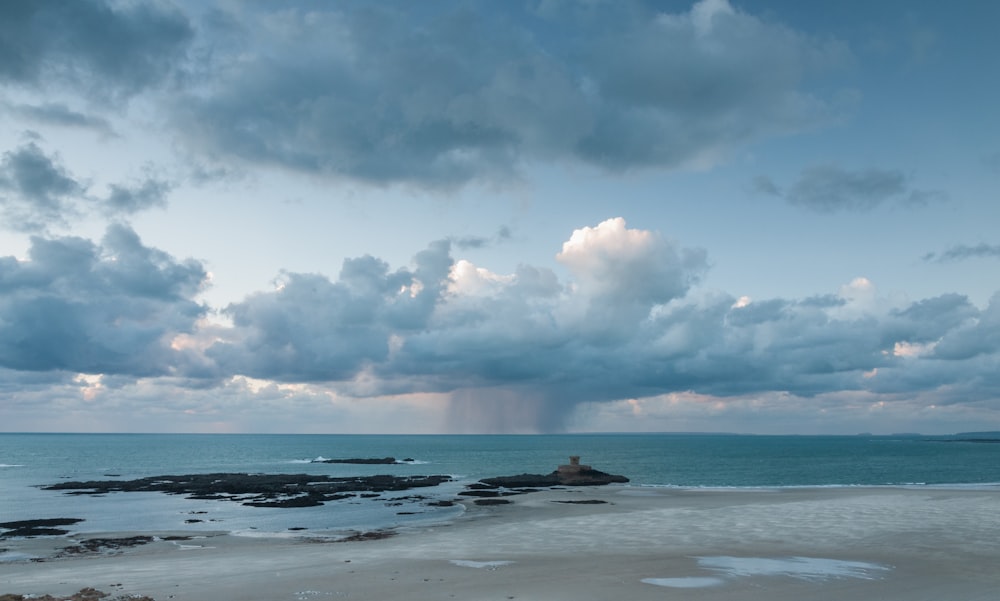 a cloudy sky over the ocean with a person sitting on a rock