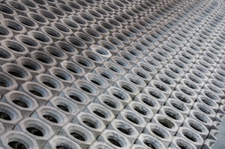 A pattern of hexagonal concrete blocks arranged in a repetitive grid. Each block has a circular opening in the center and they are placed closely together, creating a sense of depth and symmetry.