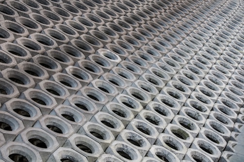 A pattern of hexagonal concrete blocks arranged in a repetitive grid. Each block has a circular opening in the center and they are placed closely together, creating a sense of depth and symmetry.