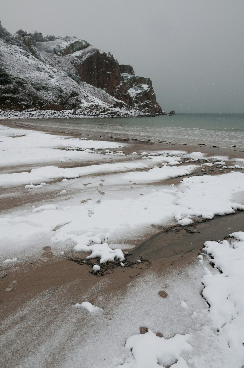 a sandy beach covered in snow next to a mountain