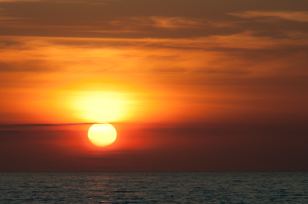 the sun is setting over the ocean on a cloudy day