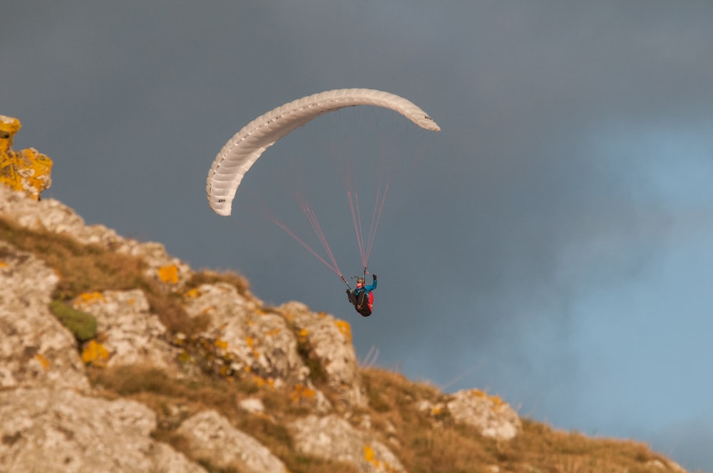 a person paragliding over a rocky hill under a cloudy sky