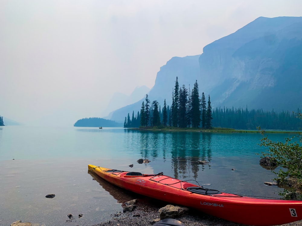 a red kayak sitting on the shore of a lake