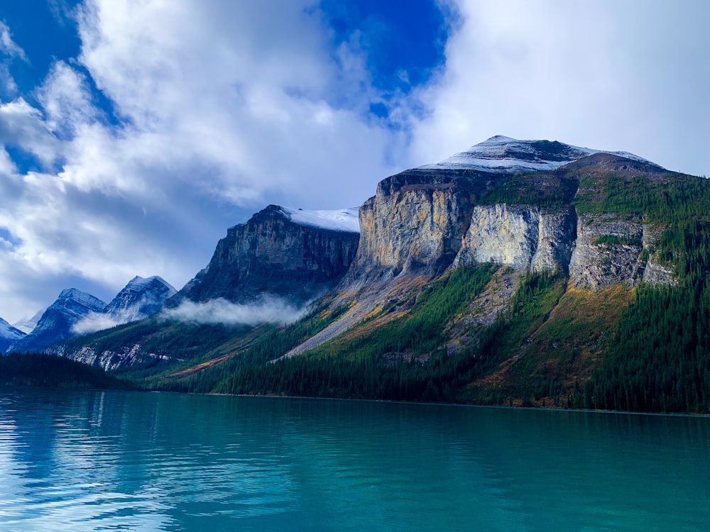 a mountain with snow on top of it and a body of water below