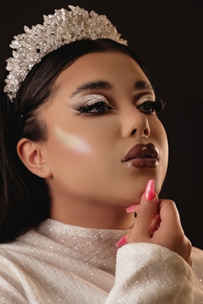 Close-up of a smiling queen wearing a sparkling crown and vibrant makeup.