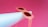 A pair of stylish, translucent pink sunglasses rests atop a white cylindrical object, set against a vibrant pink background. The sunglasses have a retro feel, with oversized frames and dark lenses.