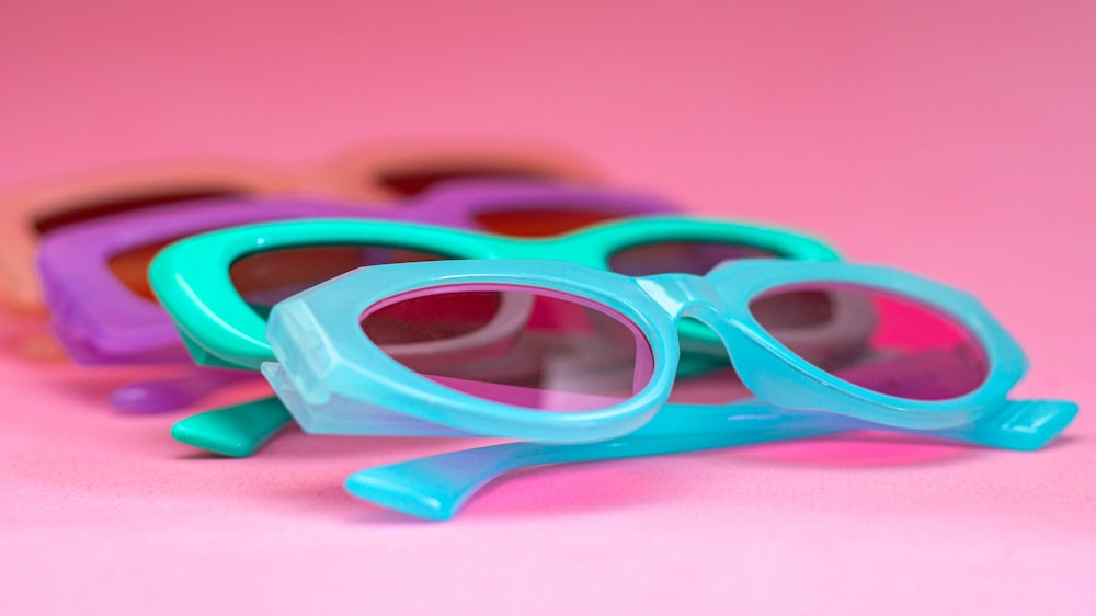 three pairs of sunglasses laying on a pink surface
