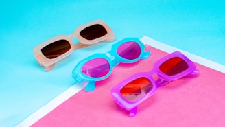 A pair of retro square sunglasses with a colorful background.