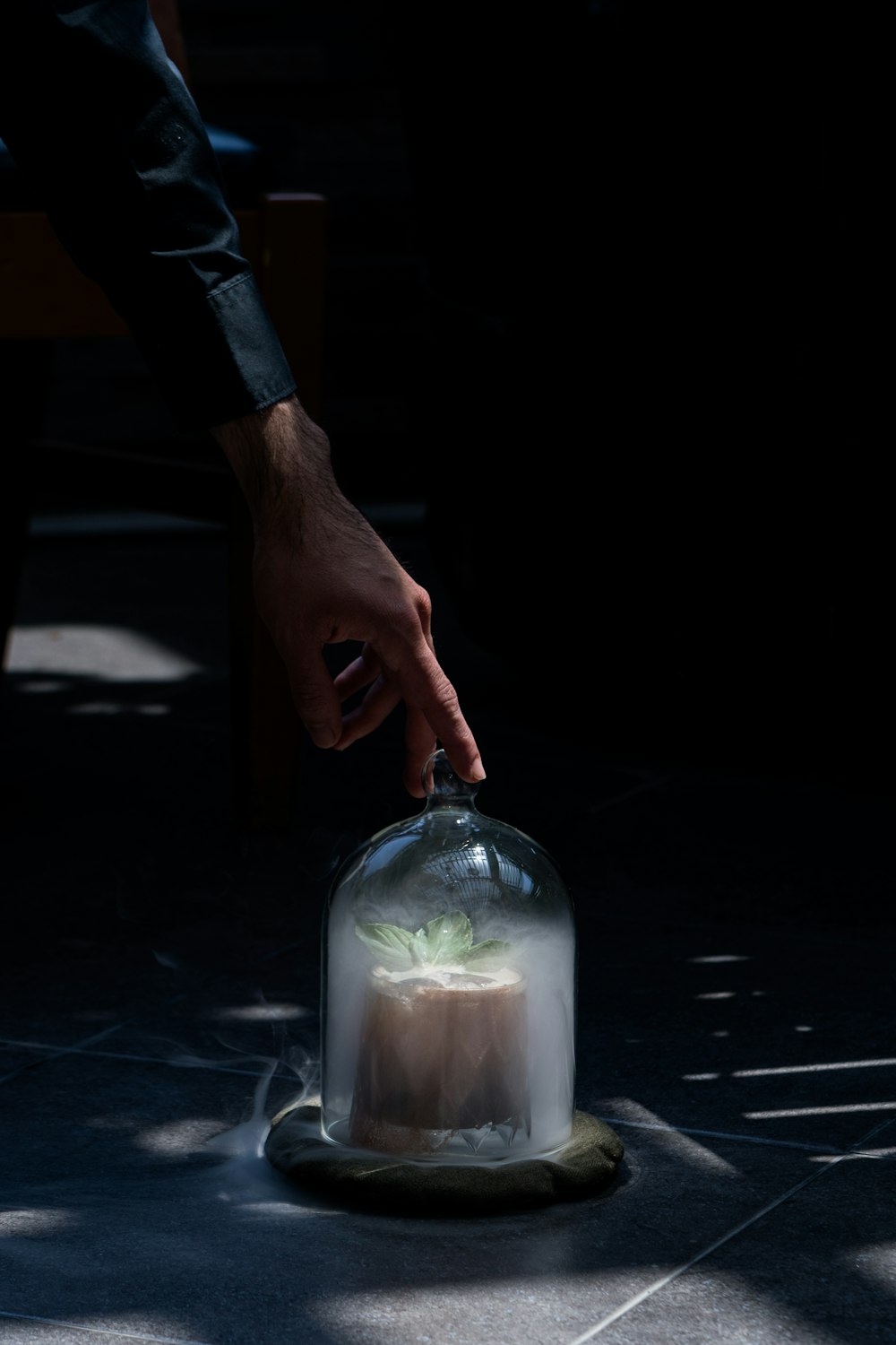 a person reaching for a cake under a glass dome