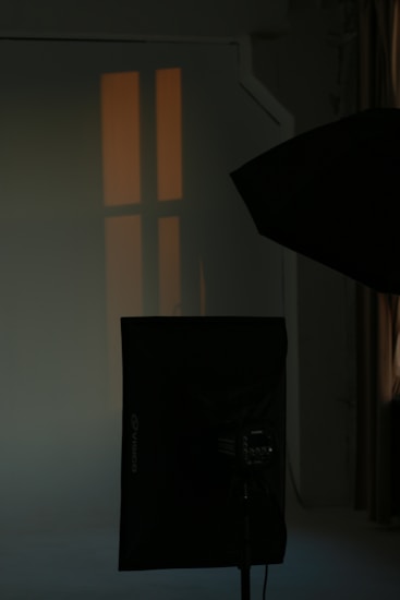 A dimly lit studio setup with a softbox light and a faint window reflection on the wall. The atmosphere is calm with muted colors and minimal lighting, creating a serene and introspective mood.