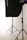 A photo studio setup featuring a black softbox on a stand, with another light stand visible in the background. The scene is minimalistic with clean, white surroundings.