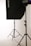 A photo studio setup featuring a black softbox on a stand, with another light stand visible in the background. The scene is minimalistic with clean, white surroundings.
