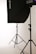 A photo studio setup featuring a black softbox on a stand, with another light stand visible in the background. The scene is minimalistic with clean, white surroundings.