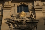 An ornate architectural detail featuring a relief with angelic figures surrounding a golden triangle with an eye at its center, mounted on a classical building facade.
