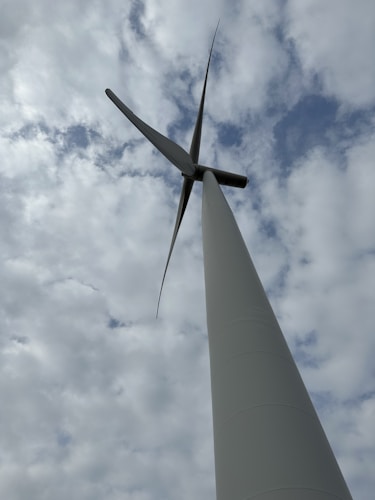 A wind turbine with three blades is shown from a low angle against a cloudy sky, conveying a sense of height and scale.