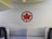 A red maple leaf logo is mounted on a wall with a textured pattern, located within an airplane cabin. The seating area features modern design elements and neutral colors.