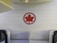 A red maple leaf logo is mounted on a wall with a textured pattern, located within an airplane cabin. The seating area features modern design elements and neutral colors.