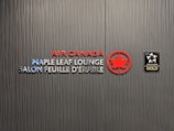 A textured wall featuring the logos and text for Air Canada Maple Leaf Lounge and Star Alliance Gold. The text includes bilingual English and French, with the Air Canada logo prominently displayed in red next to a stylized maple leaf.
