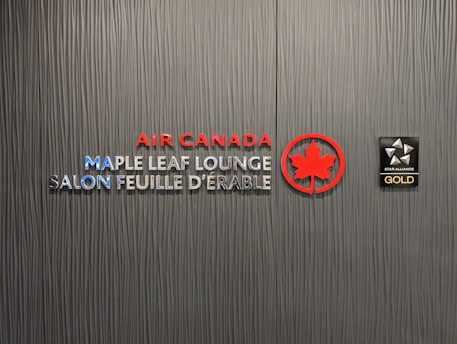 A textured wall featuring the logos and text for Air Canada Maple Leaf Lounge and Star Alliance Gold. The text includes bilingual English and French, with the Air Canada logo prominently displayed in red next to a stylized maple leaf.