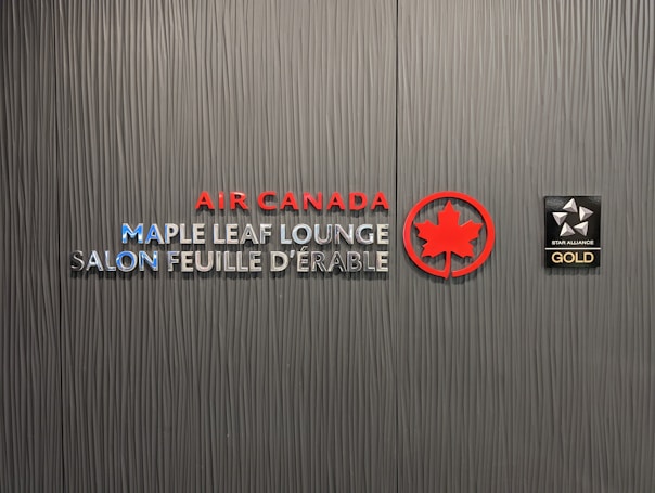 A textured wall featuring the logos and text for Air Canada Maple Leaf Lounge and Star Alliance Gold. The text includes bilingual English and French, with the Air Canada logo prominently displayed in red next to a stylized maple leaf.