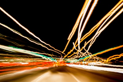 Long exposure photograph capturing light trails of various colors against a dark background. The streaks of light create a dynamic and energetic pattern, suggesting motion and speed.