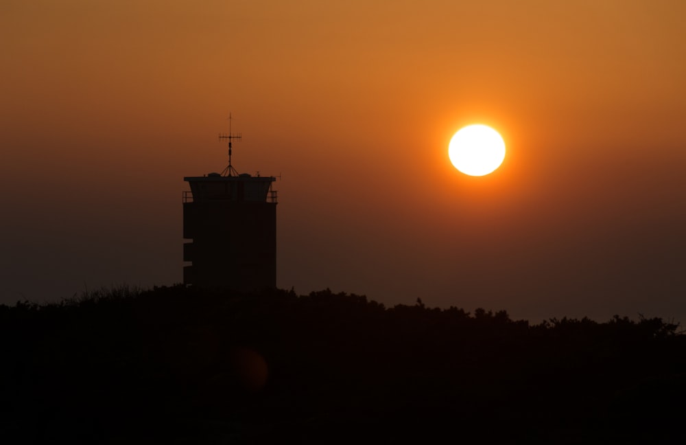 Die Sonne geht hinter einem Turm auf einem Hügel unter