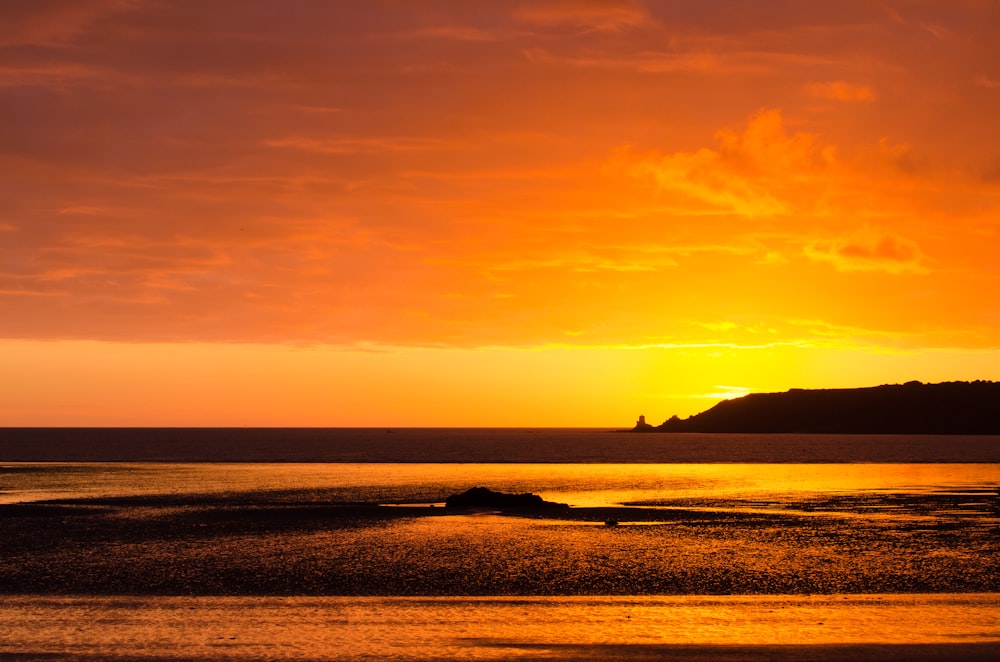 the sun is setting over the ocean with a small island in the distance