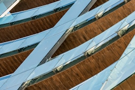 A pattern of diagonally intersecting glass and wooden slats creates a modern architectural element. The glass appears to have a blue tint and reflects light, while the wooden sections provide a contrasting warm tone.