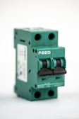 A green electrical circuit breaker with two switches is shown from a side angle. The breaker has visible text and labels, including 'FPV-63' and 'C32'. The overall design is boxy with two black switches and multiple openings for wiring connections.