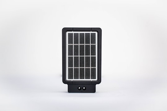 A small, rectangular solar panel device with a grid-like pattern of photovoltaic cells encased in a black frame. It is set against a clean, white background.