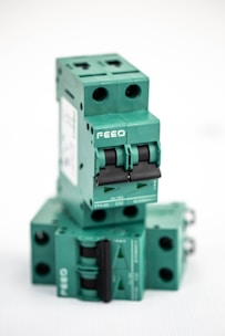 A stacked arrangement of multiple green electrical circuit breakers, each with a double switch mechanism and labeled with the brand 'FEEO'. The breakers have a boxy shape with round openings for connections.