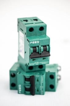 A stacked arrangement of multiple green electrical circuit breakers, each with a double switch mechanism and labeled with the brand 'FEEO'. The breakers have a boxy shape with round openings for connections.