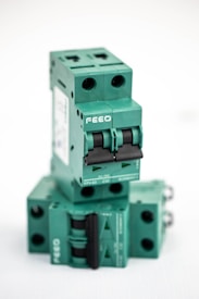 A stacked arrangement of multiple green electrical circuit breakers, each with a double switch mechanism and labeled with the brand 'FEEO'. The breakers have a boxy shape with round openings for connections.