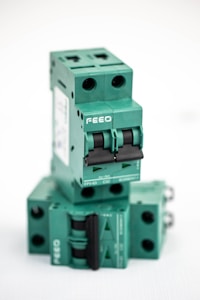 A stacked arrangement of multiple green electrical circuit breakers, each with a double switch mechanism and labeled with the brand 'FEEO'. The breakers have a boxy shape with round openings for connections.