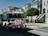 A fire truck labeled S.F.F.D is parked on a residential street with classic Victorian-style homes in the background. The street is sunny and lined with trees. Sidewalks are visible alongside the parked vehicles.