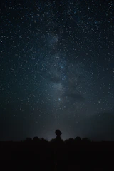 A starry sky with a silhouette of a person looking up at a UFO