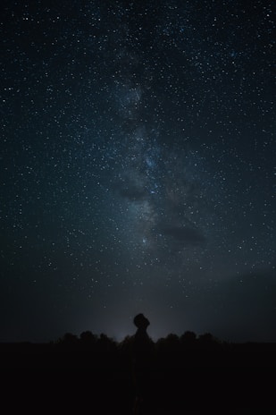 A serene night sky filled with stars and a glowing silhouette of a person looking upward.