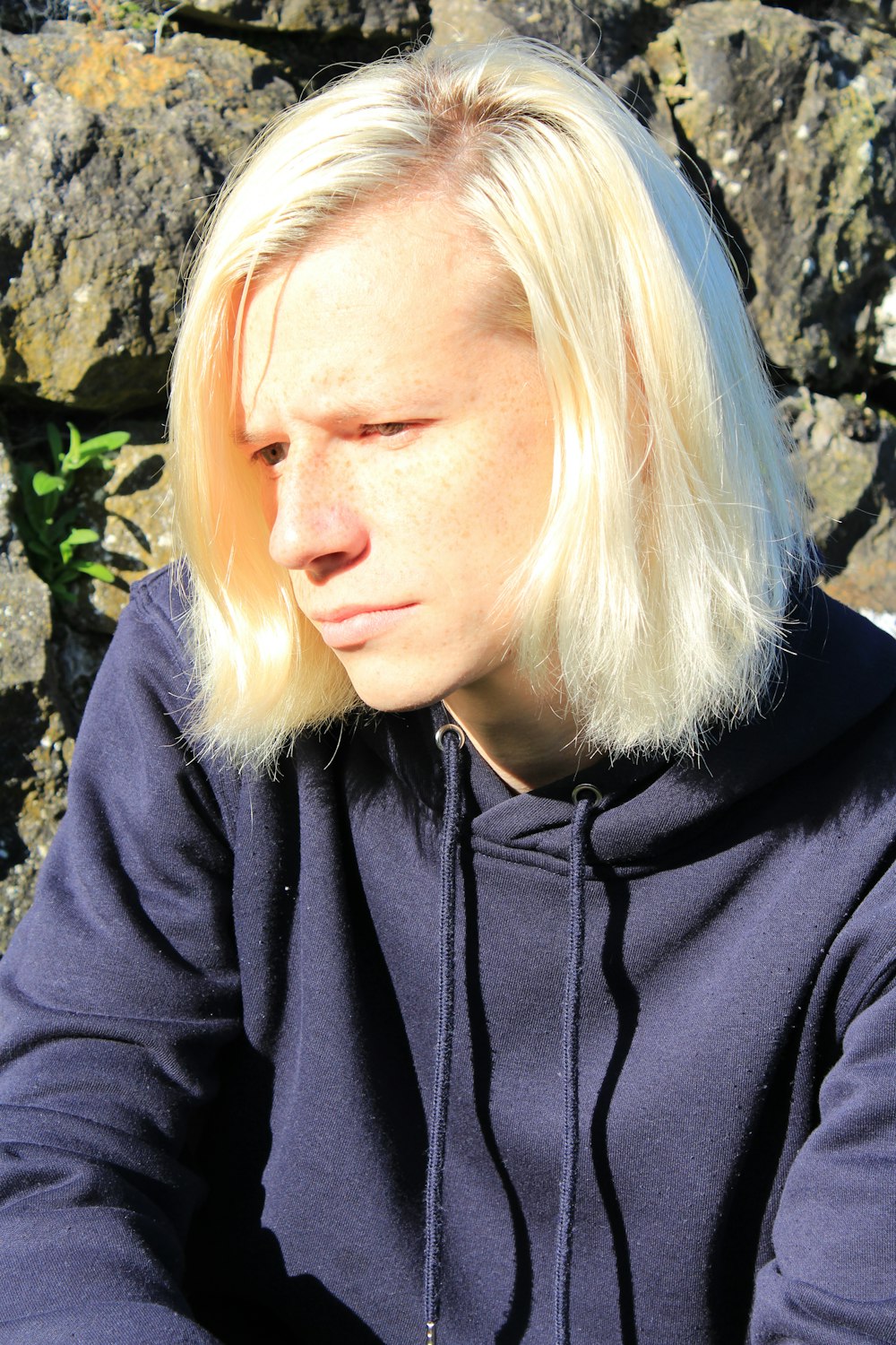 a blonde haired woman sitting in front of a rock wall