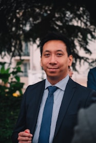 a man in a suit and tie standing in front of a tree
