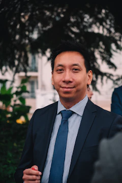 a man in a suit and tie standing in front of a tree