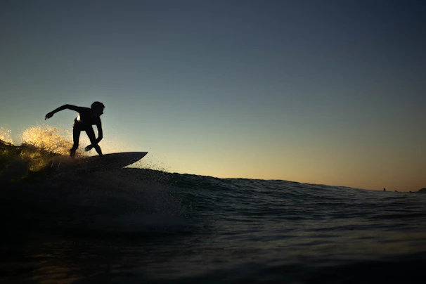 Surfer catching a wave at Playa de La Laja during a vibrant sunset.