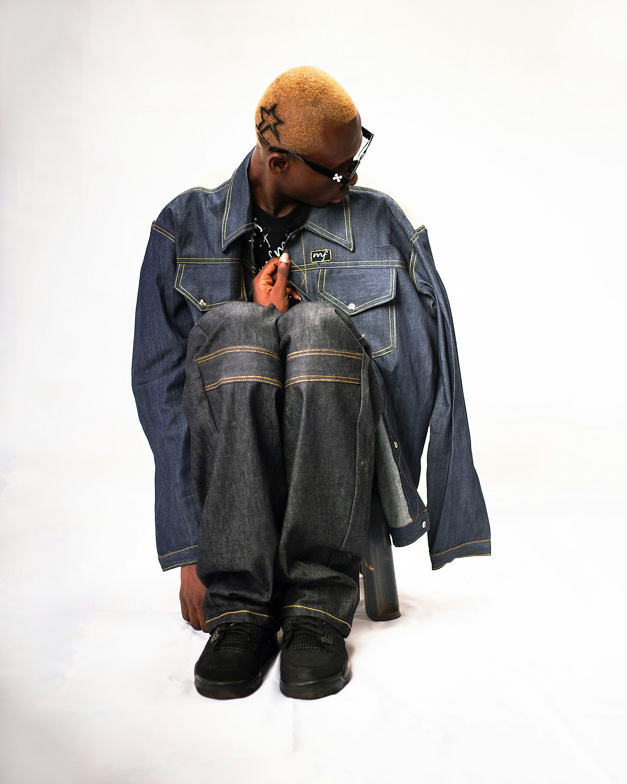 Un jeune homme assis par terre vêtu d’une veste en jean