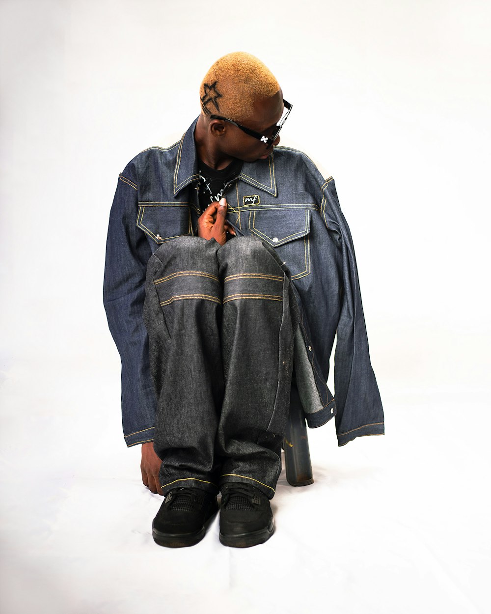 a young man sitting on the ground wearing a jean jacket