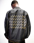 Denim jacket with a large back embroidery of a laughing marijuana bud holding a lighter.